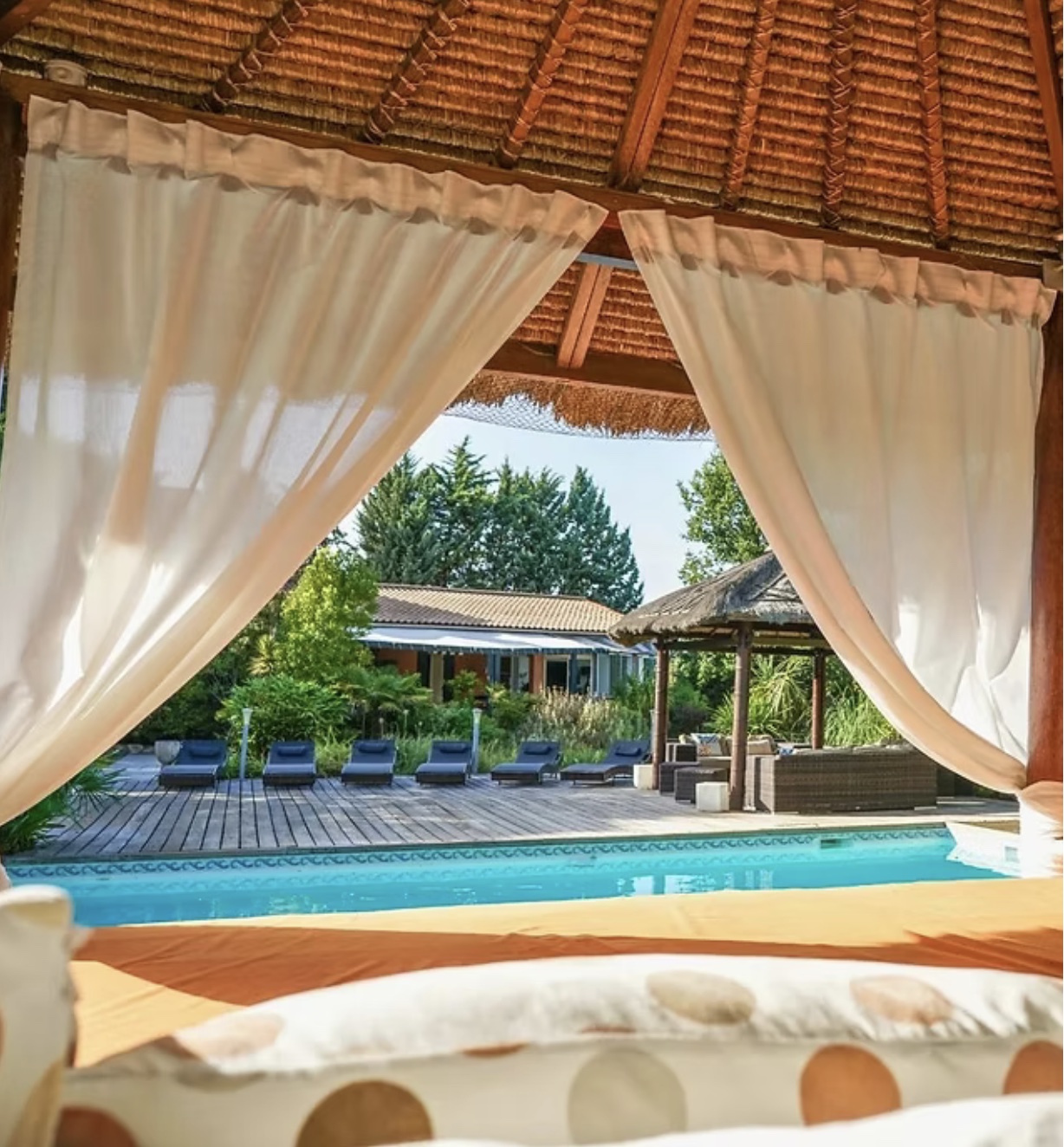 Poolside daybed with white curtains, loungers, and a garden